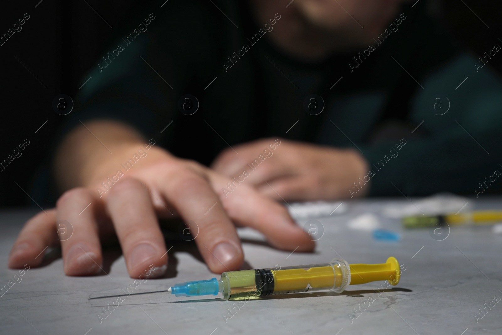 Photo of Overdosed man at grey table, focus on syringe with drugs