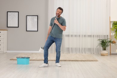 Photo of Happy man in headphones with mop singing while cleaning at home