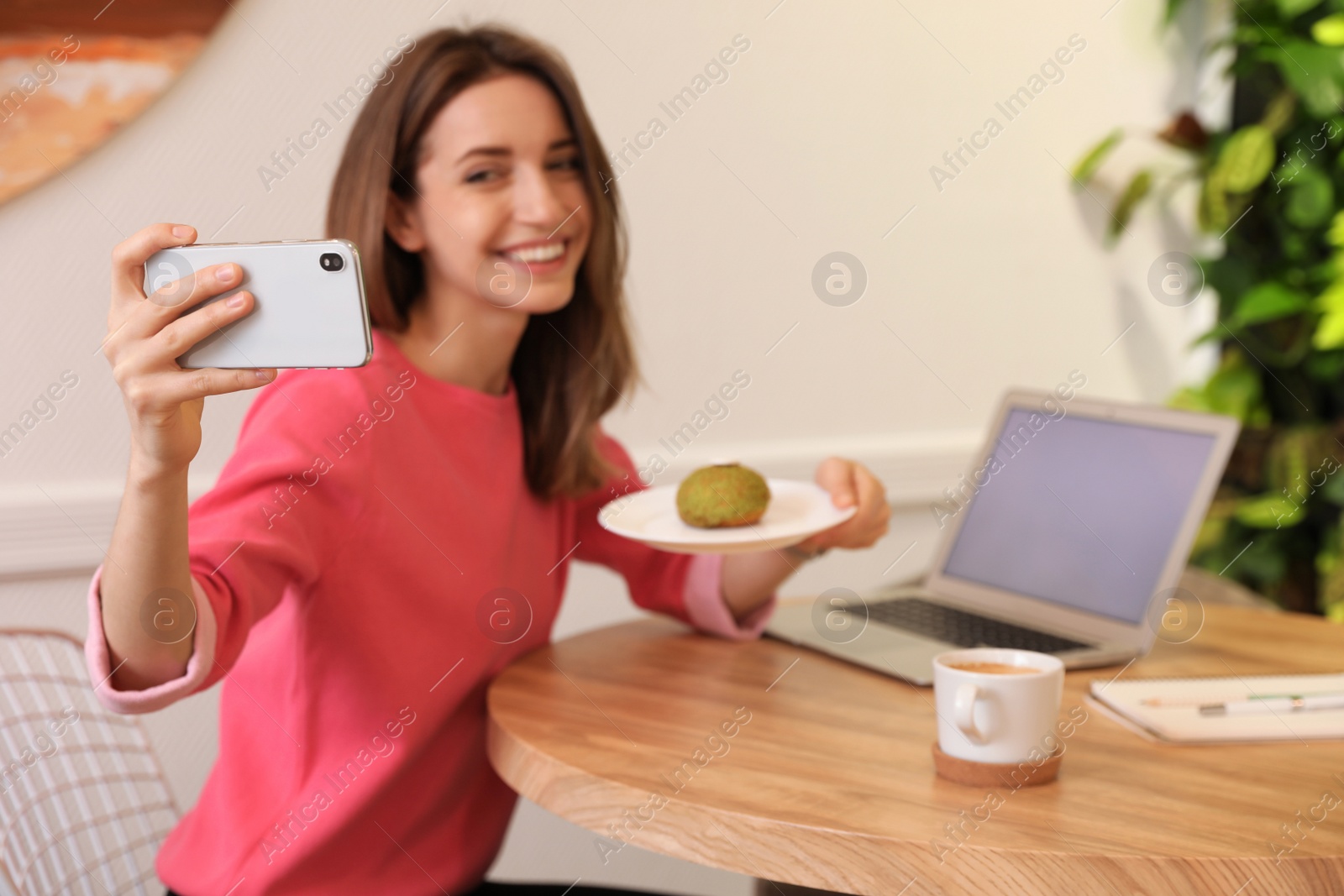 Photo of Young blogger taking selfie at table in cafe