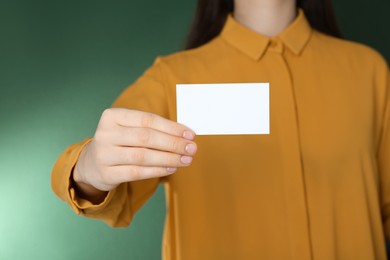 Woman holding white business card on green background, closeup