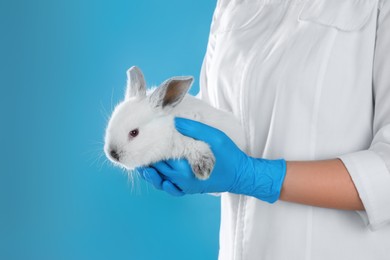 Photo of Scientist holding rabbit on light blue background, closeup. Animal testing concept