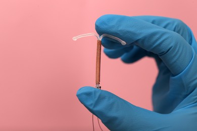 Photo of Doctor holding T-shaped intrauterine birth control device on pink background, closeup. Space for text