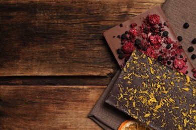 Photo of Different chocolate bars with freeze dried fruits on wooden table, flat lay. Space for text