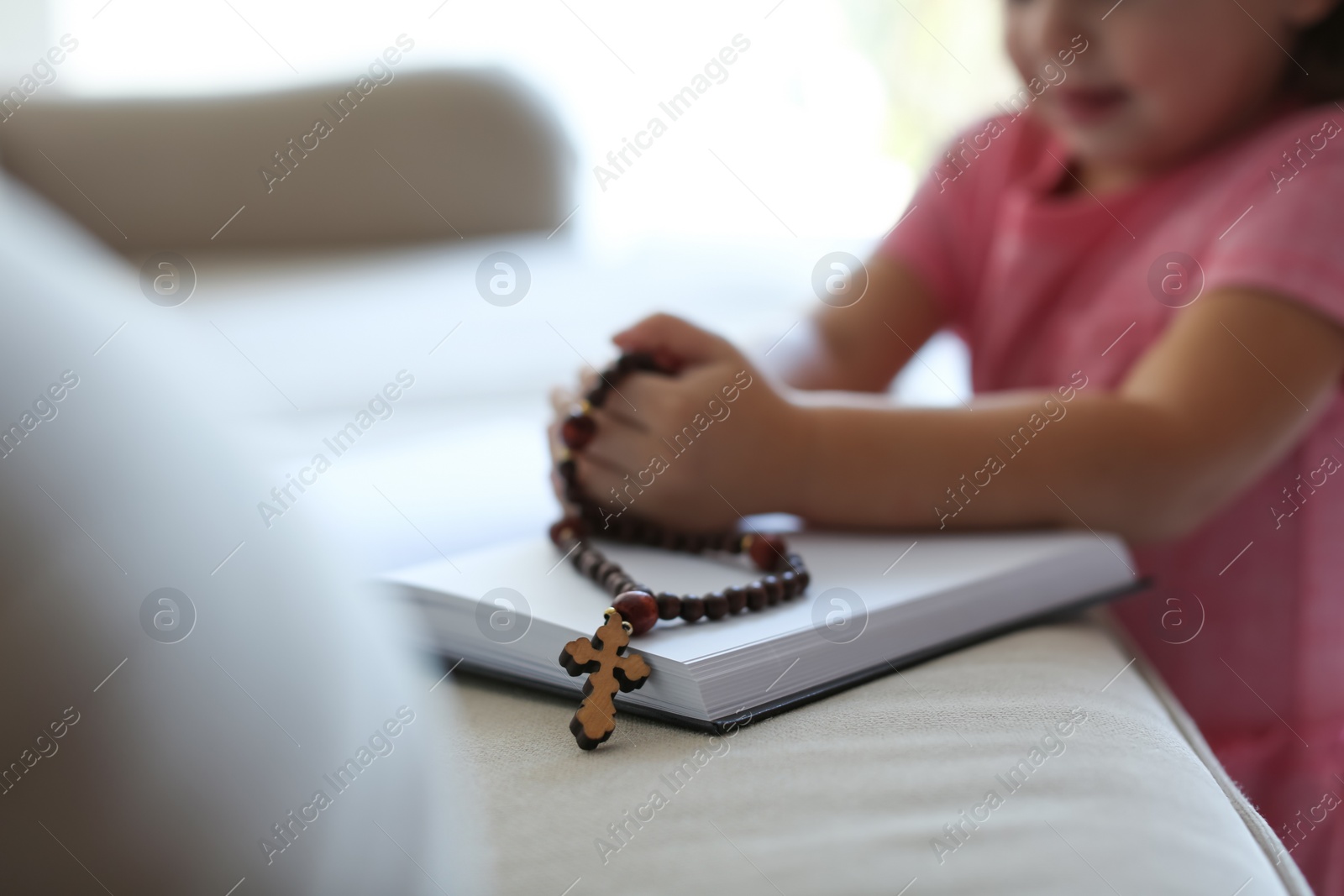 Photo of Cute little girl with beads praying over Bible at home