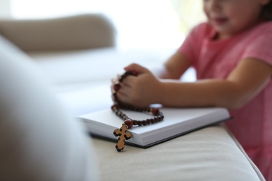 Cute little girl with beads praying over Bible at home