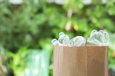 Photo of Used plastic bottles in paper bag on blurred background, space for text. Recycling problem