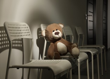 Photo of Cute lonely teddy bear on chair in dark room