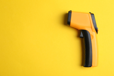 Photo of Modern non-contact infrared thermometer on yellow background, top view. Space for text