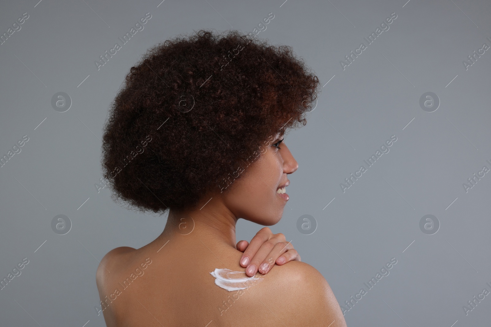 Photo of Beautiful young woman applying body cream onto back on grey background