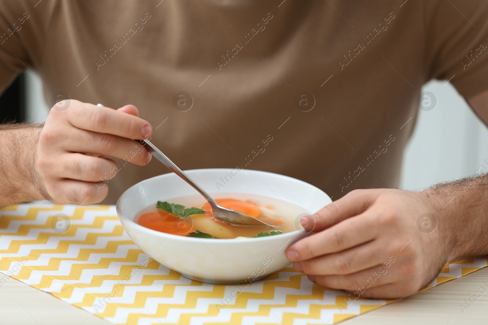 Photo of Young man eating tasty vegetable soup at table, closeup