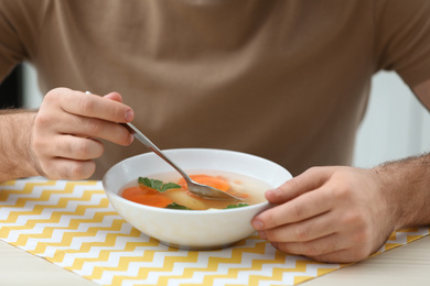 Young man eating tasty vegetable soup at table, closeup