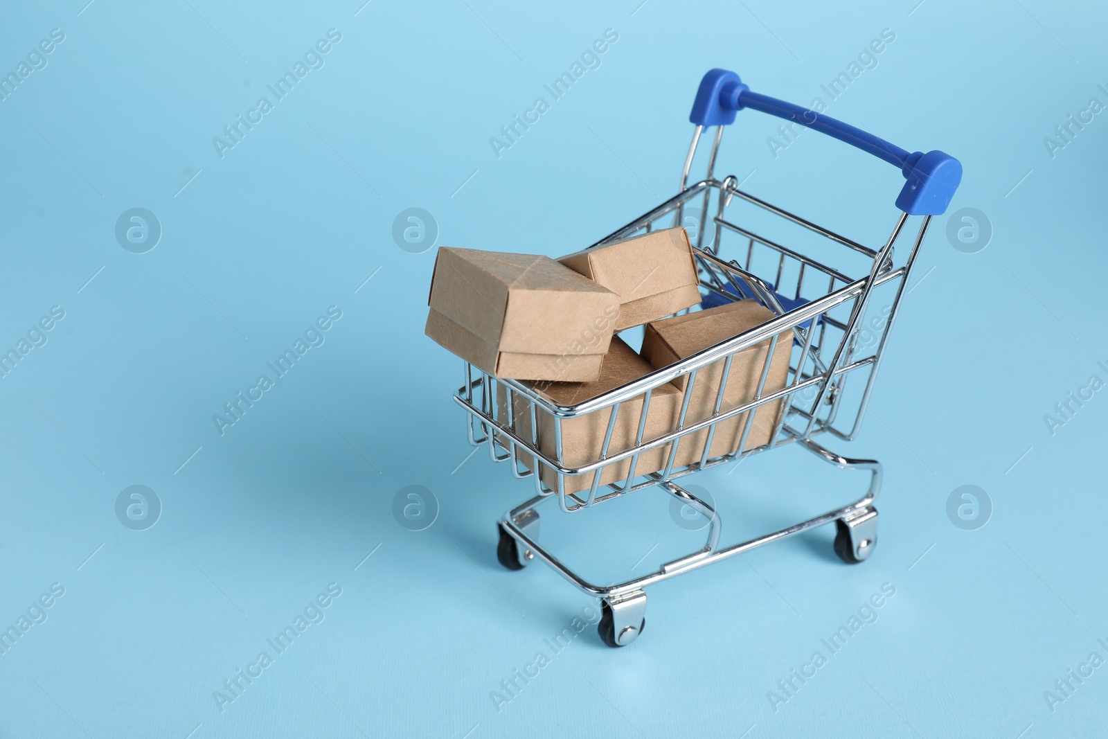 Photo of Small metal shopping cart with cardboard boxes on light blue background, space for text