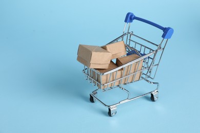 Photo of Small metal shopping cart with cardboard boxes on light blue background, space for text
