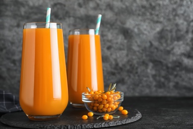 Delicious sea buckthorn juice and fresh berries on black table against grey background. Space for text