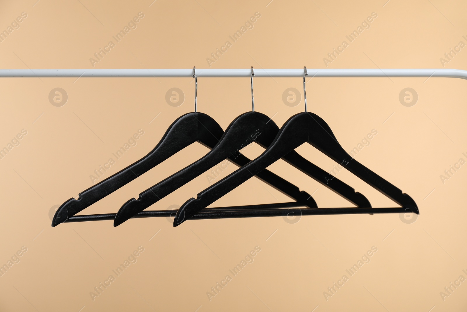 Photo of Black clothes hangers on rack against beige background