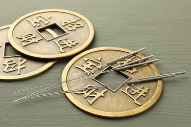 Acupuncture needles and antique Chinese coins on grey wooden table, closeup