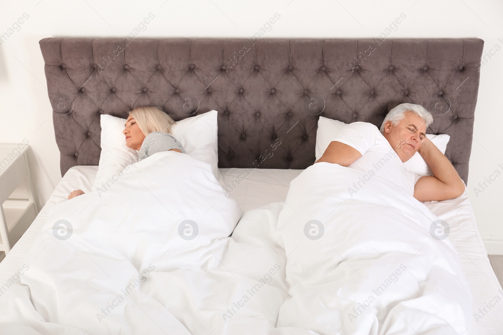 Photo of Mature couple sleeping back to back in bed at home. Relationship problems