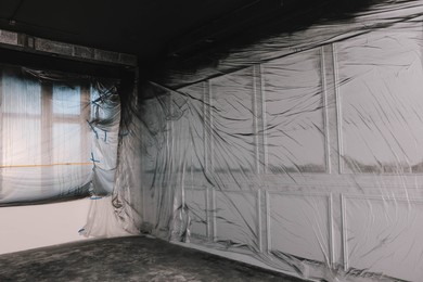 Windows and wall covered with plastic film in empty room