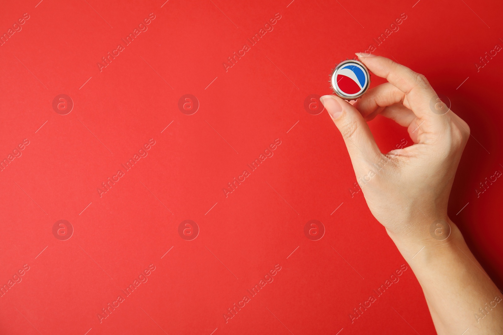 Photo of MYKOLAIV, UKRAINE - FEBRUARY 12, 2021: Woman holding Pepsi lid on red background, top view. Space for text