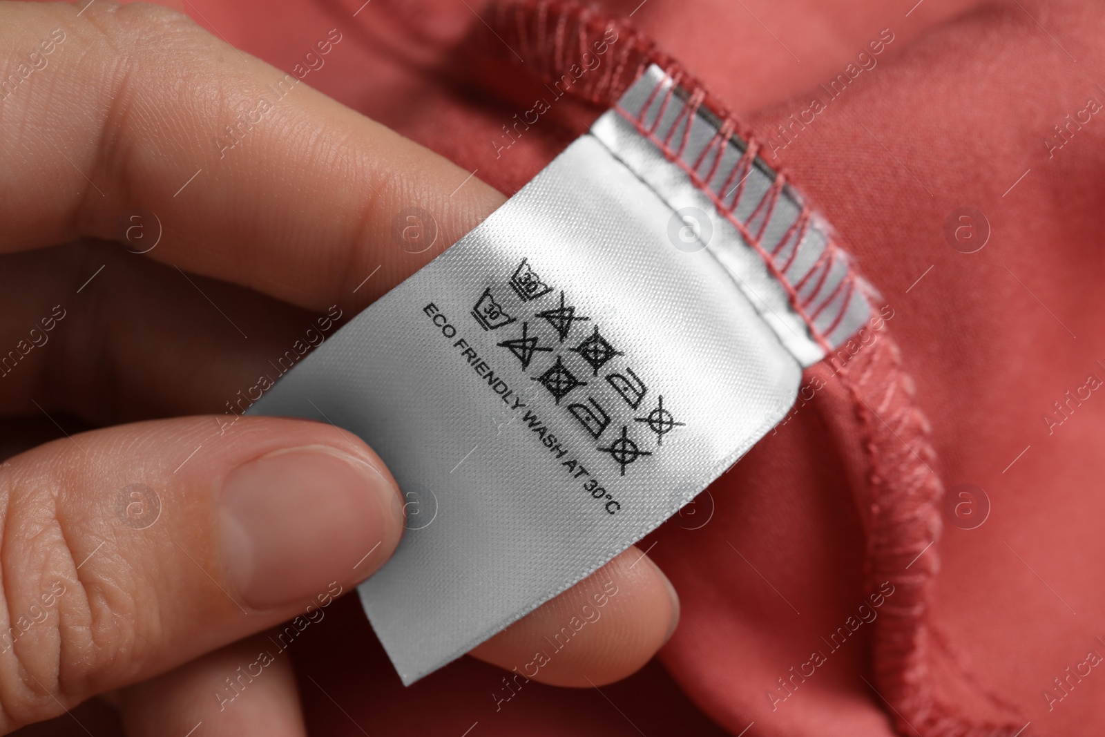 Photo of Woman holding clothing label on color garment, closeup