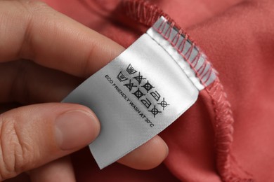 Photo of Woman holding clothing label on color garment, closeup