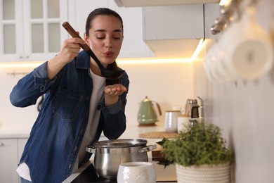 Beautiful woman with ladle tasting soup in kitchen