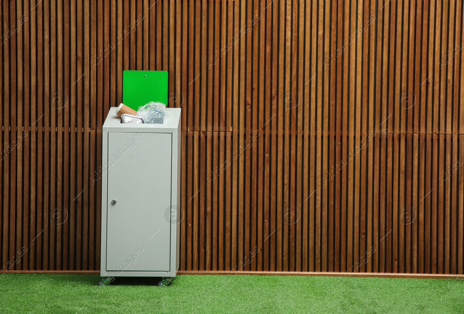 Photo of Overfilled trash bin near wooden wall indoors, space for text. Recycling concept