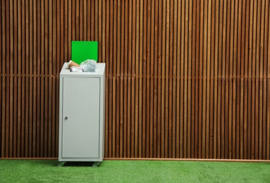 Photo of Overfilled trash bin near wooden wall indoors, space for text. Recycling concept