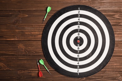 Photo of Dart board with color arrows on wooden background, top view. Space for text