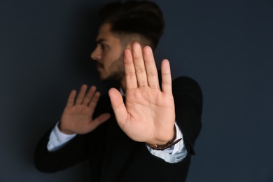 Photo of Man showing stop gesture on dark background. Problem of sexual harassment at work
