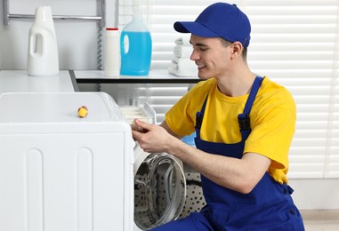 Smiling plumber repairing washing machine in bathroom