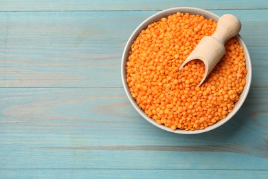 Photo of Raw red lentils and scoop in bowl on light blue wooden table, top view. Space for text