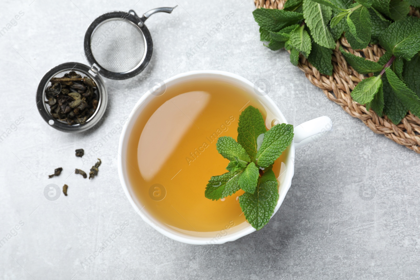 Photo of Cup of aromatic green tea with mint and dry leaves on grey table, flat lay