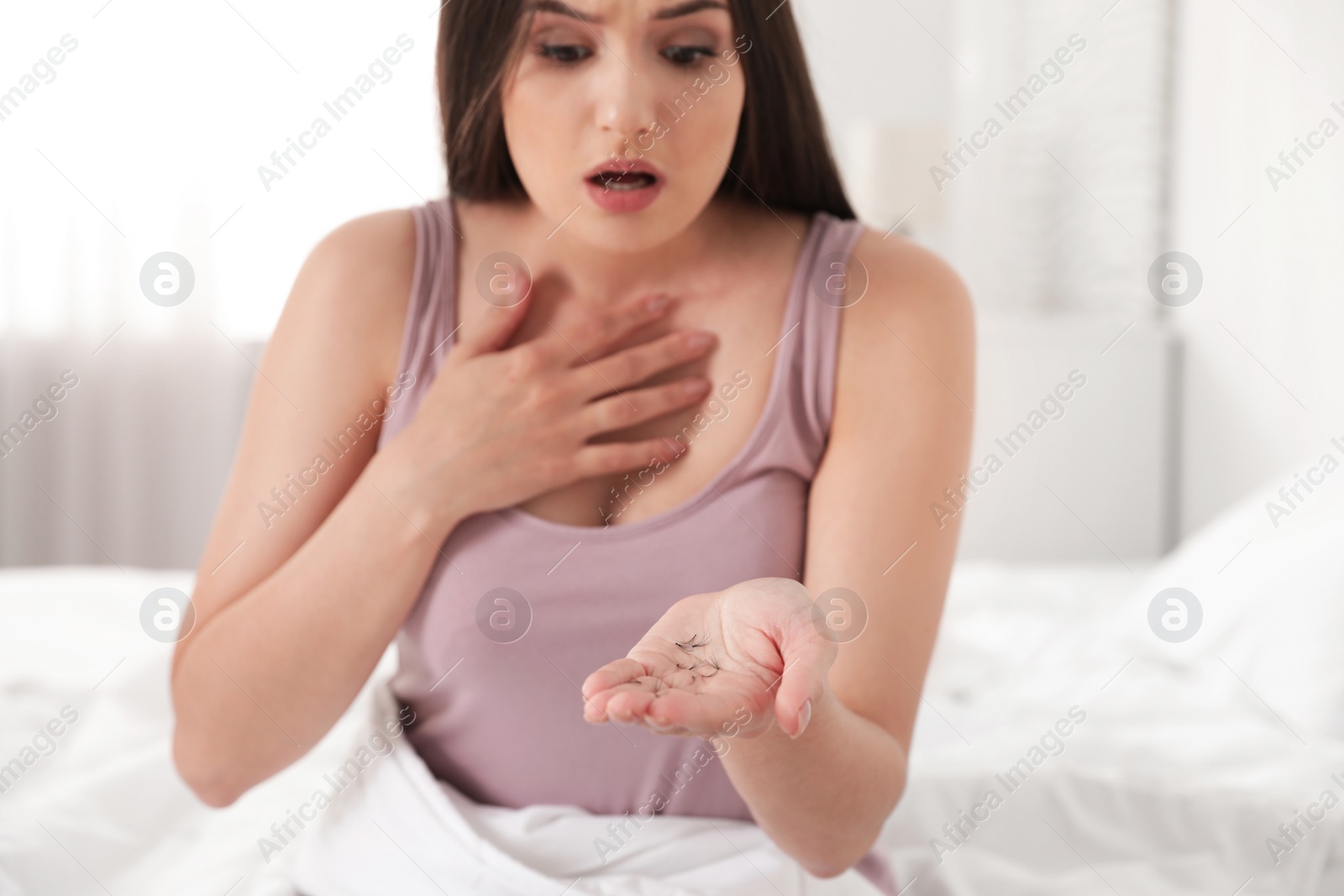 Photo of Beautiful woman holding fallen eyelashes in hand indoors