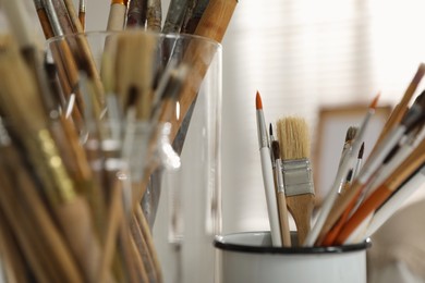 Photo of Holders with different paintbrushes in studio, closeup. Artist's workplace