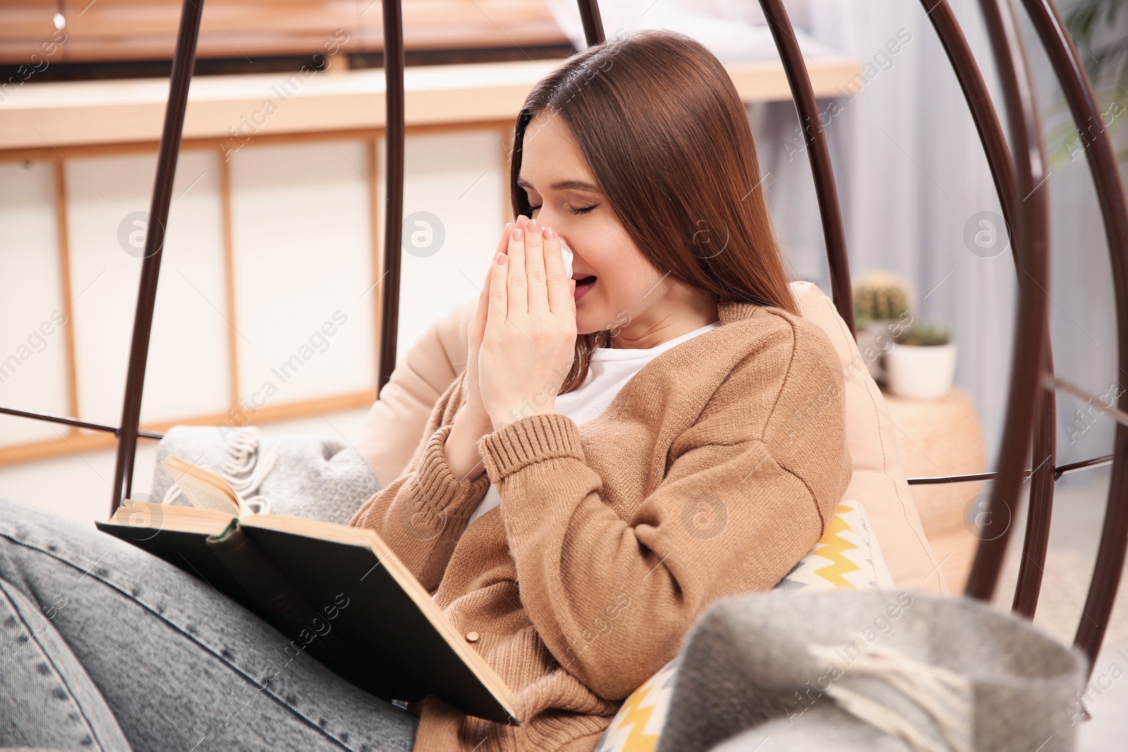 Photo of Sick young woman sneezing while reading book at home. Influenza virus