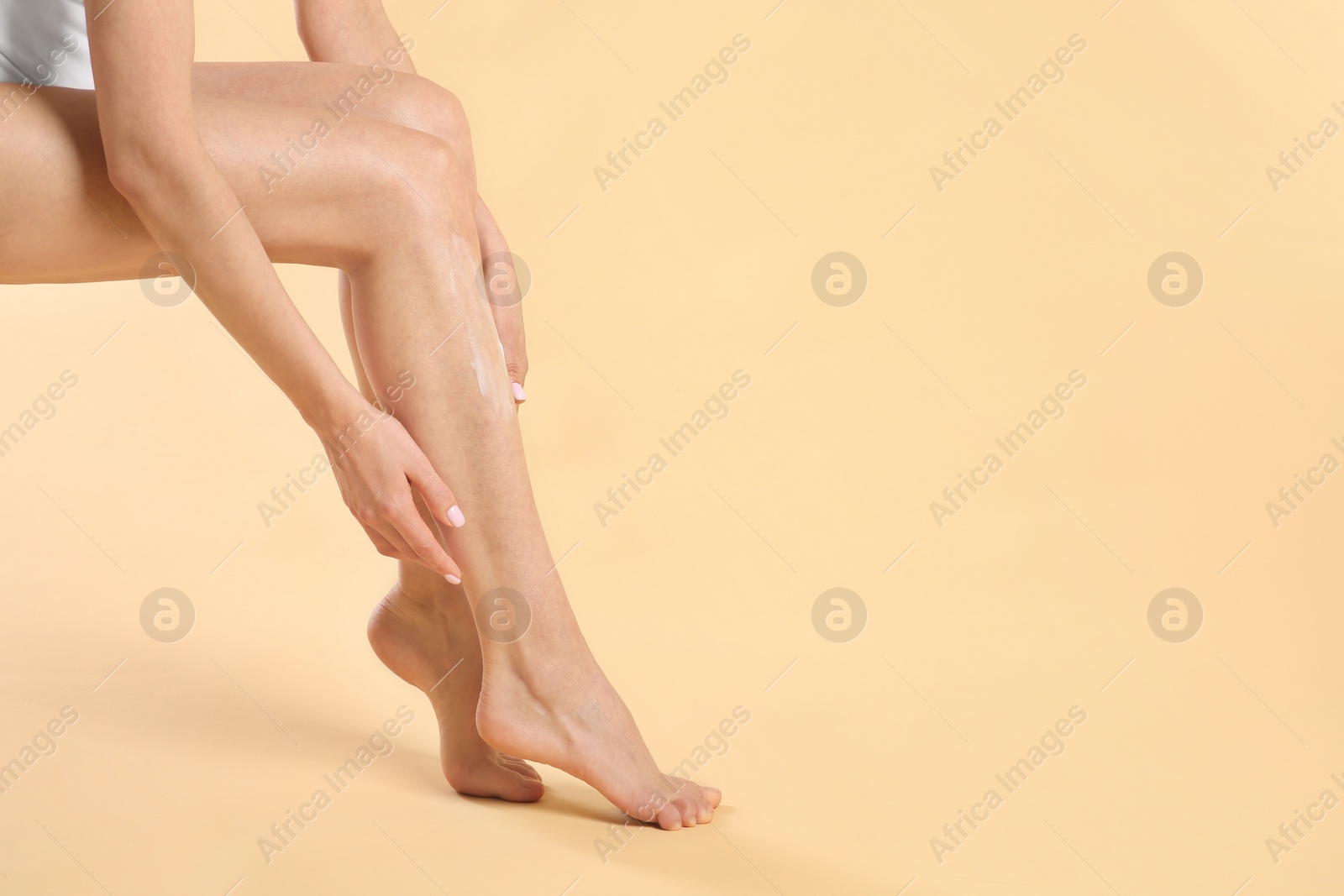 Photo of Woman applying body cream onto her smooth legs on beige background, closeup. Space for text