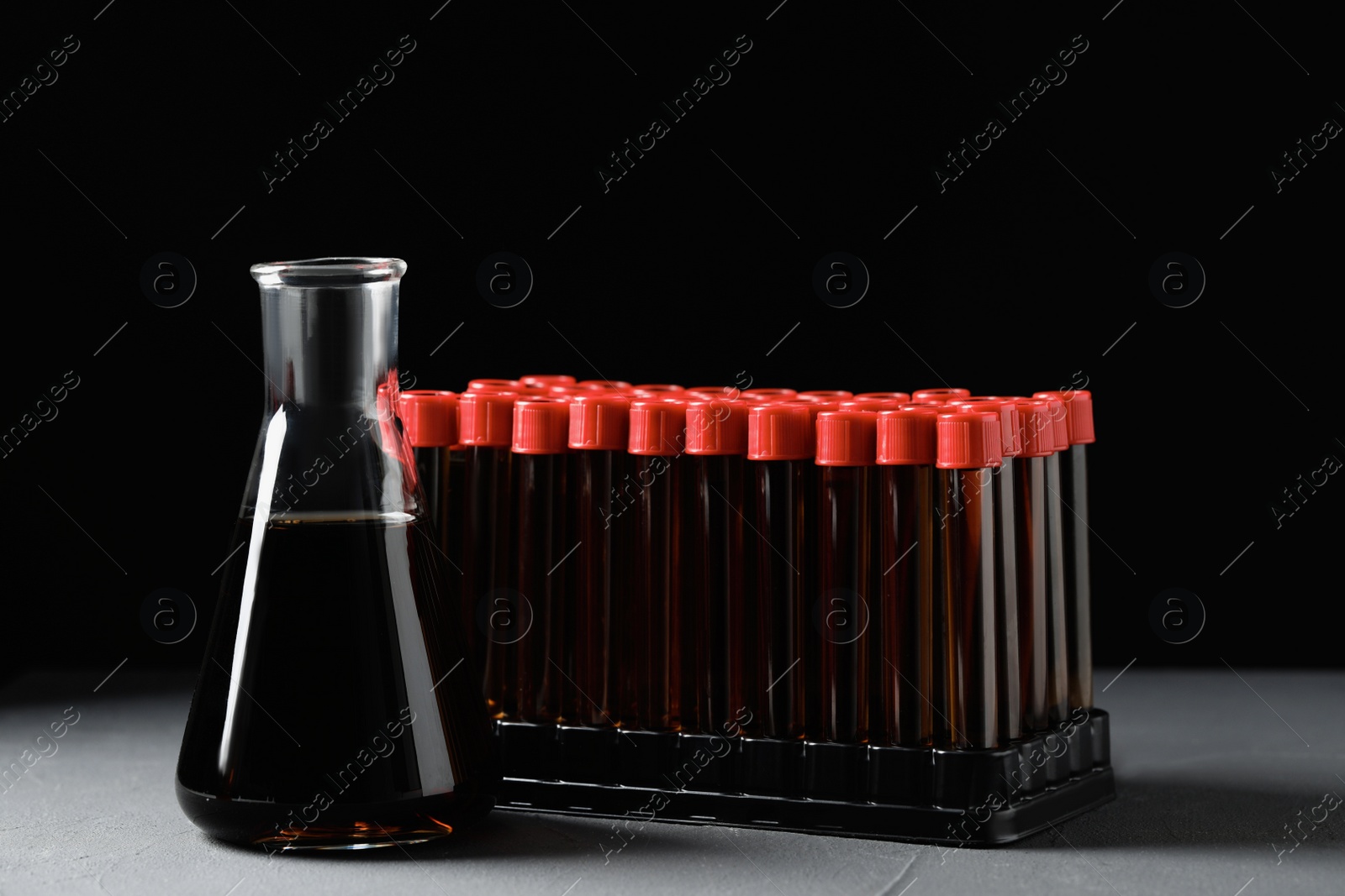 Photo of Different laboratory glassware with brown liquid on grey table against black background