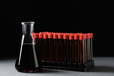 Photo of Different laboratory glassware with brown liquid on grey table against black background