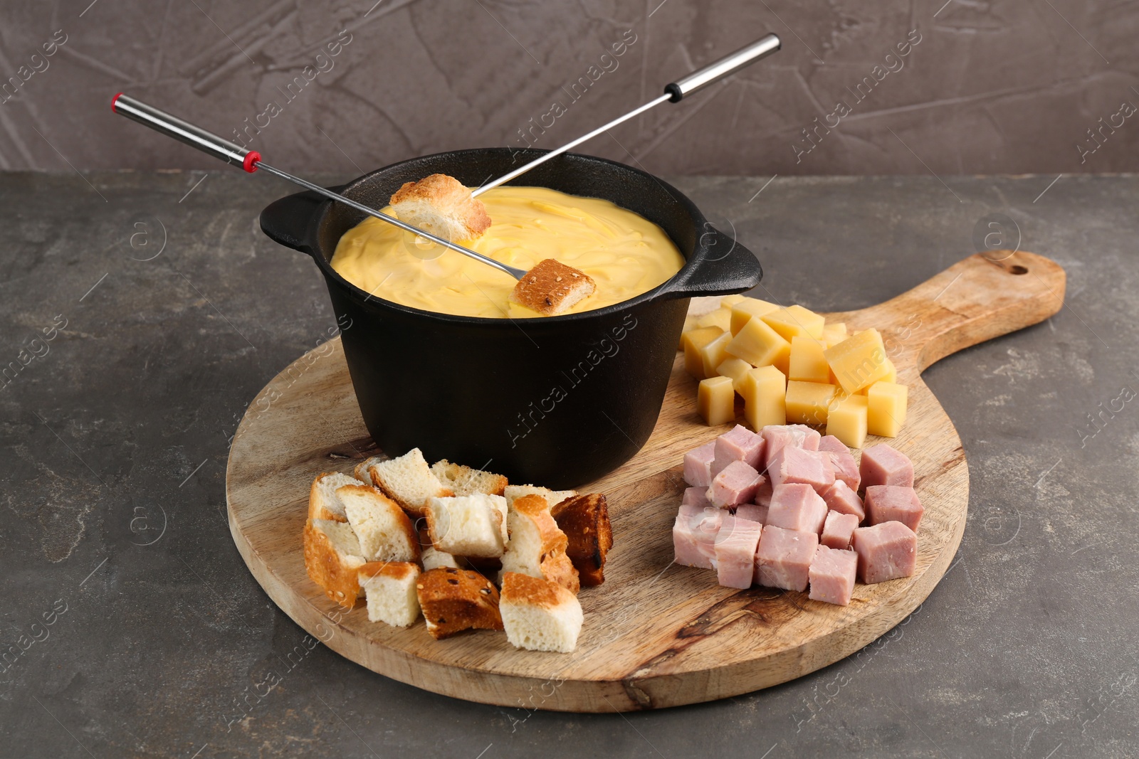 Photo of Fondue pot with tasty melted cheese, forks and different snacks on grey table