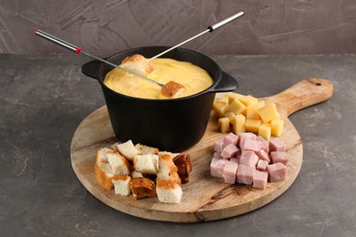 Fondue pot with tasty melted cheese, forks and different snacks on grey table