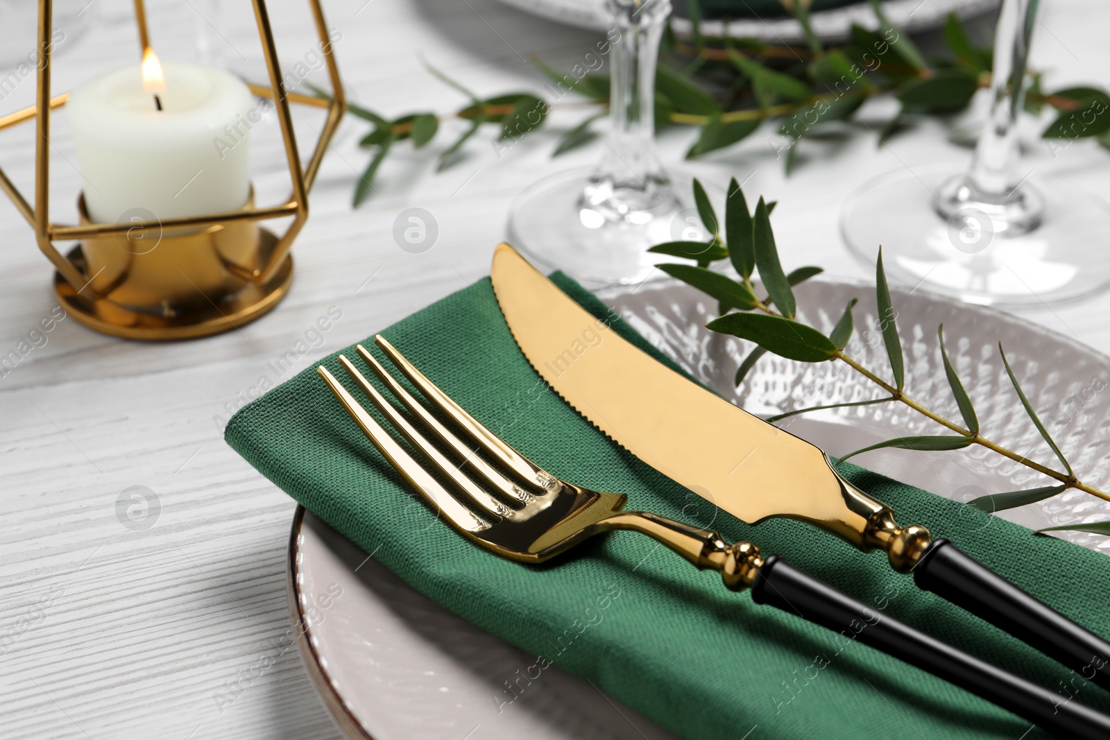 Photo of Stylish setting with cutlery and eucalyptus leaves on white wooden table, closeup