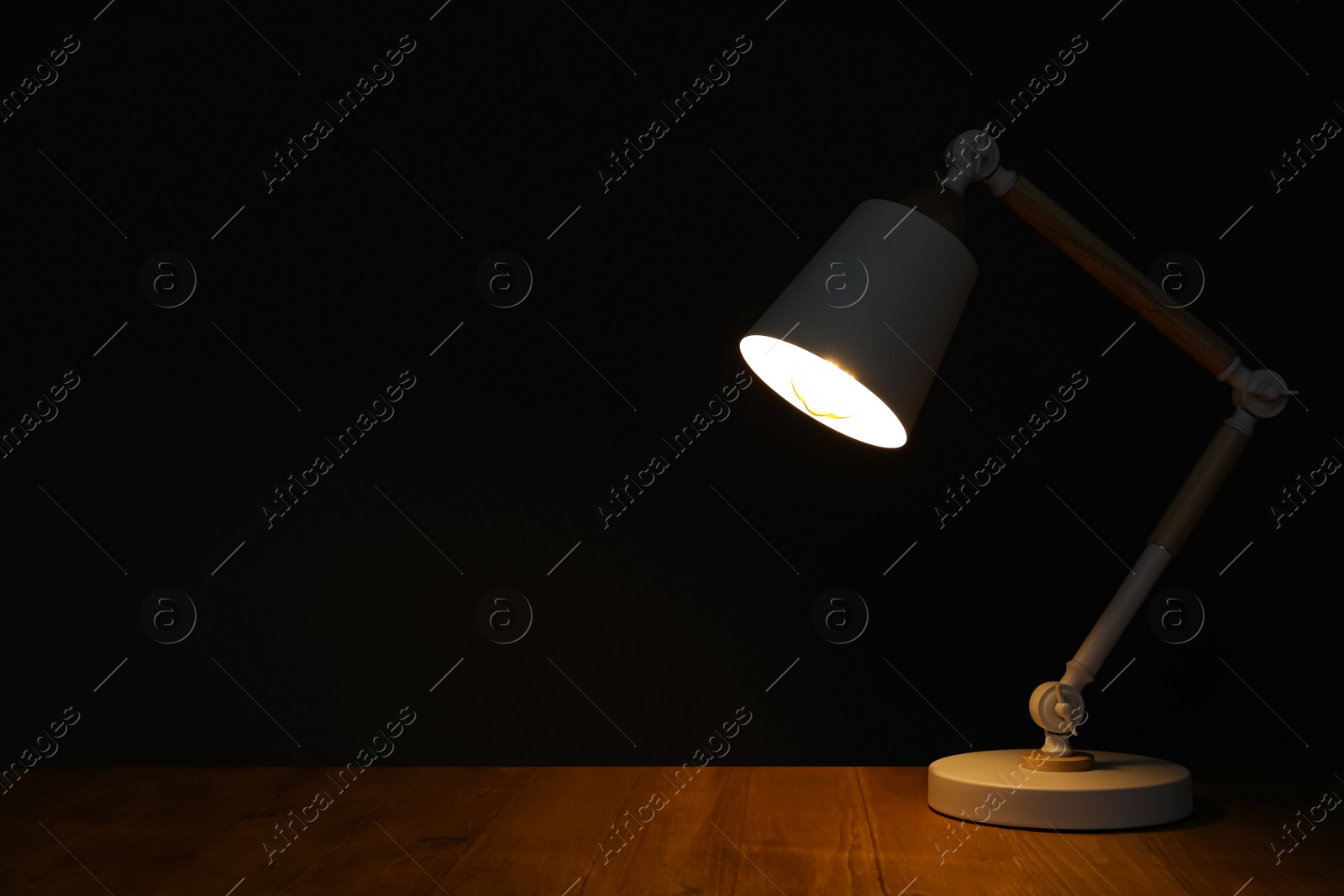 Photo of Stylish modern desk lamp on wooden table at night, space for text