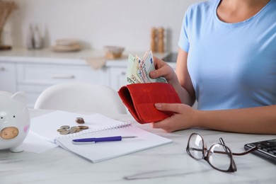 Photo of Young woman putting money into wallet at table in kitchen, closeup. Space for text