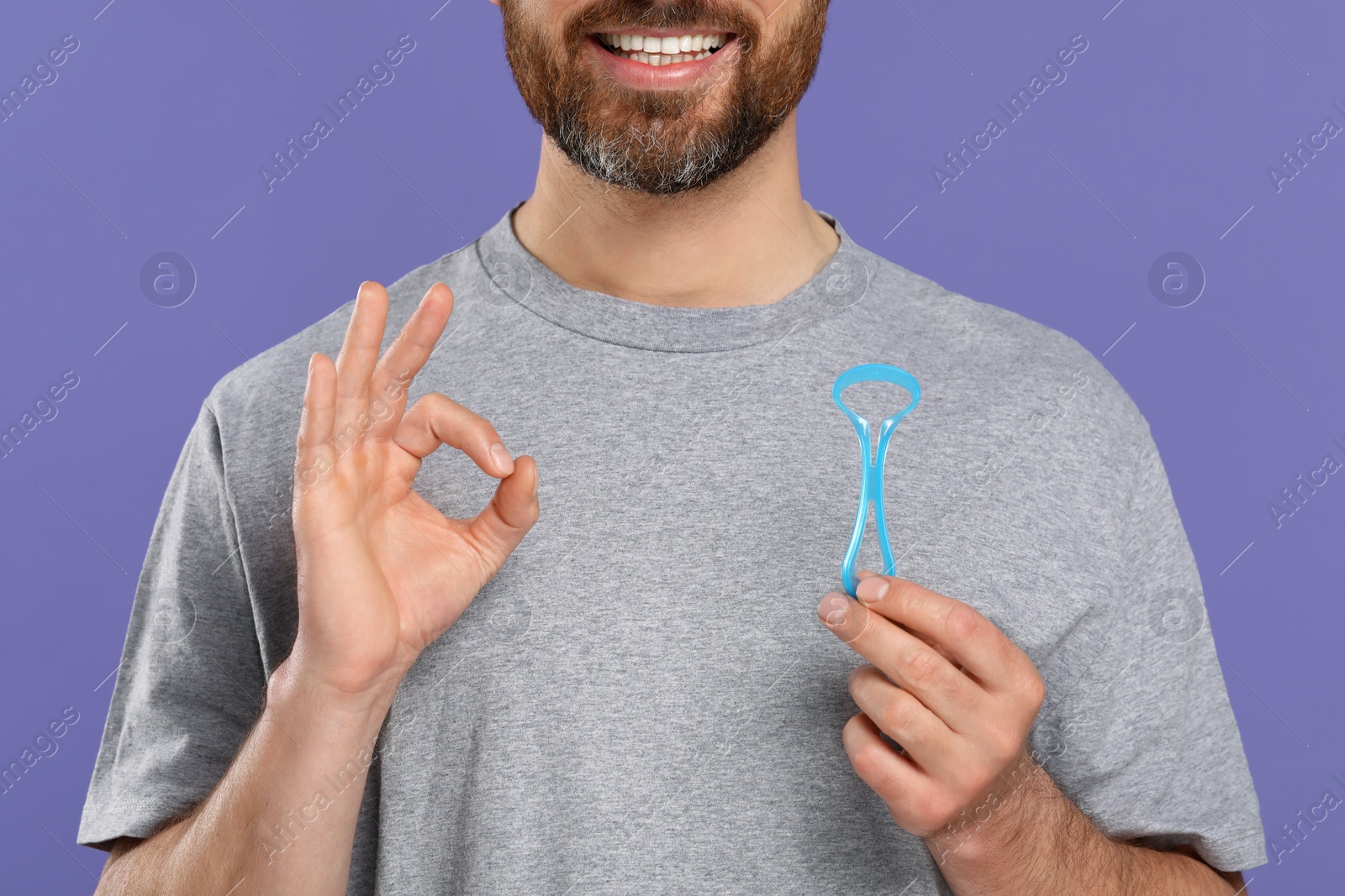 Photo of Man with tongue cleaner showing OK gesture on violet background, closeup