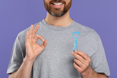 Photo of Man with tongue cleaner showing OK gesture on violet background, closeup