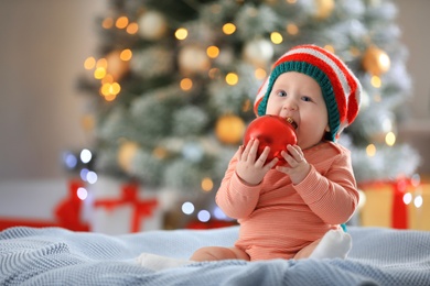 Photo of Little baby wearing elf hat on blanket indoors. First Christmas