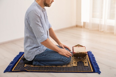 Photo of Muslim man with Koran praying on rug indoors, closeup