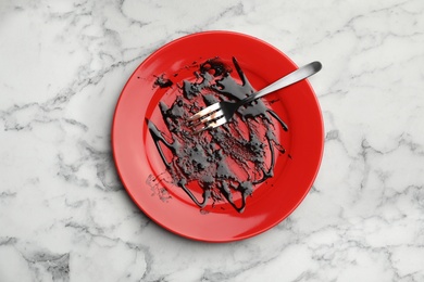 Dirty plate with food leftovers and fork on marble background, top view