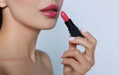 Image of Young woman with beautiful makeup holding glossy lipstick on light gray background, closeup